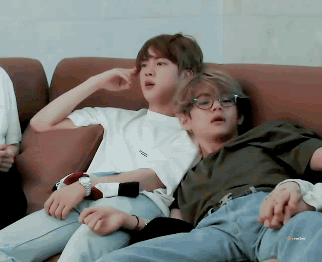 two boys are laying on a couch and one has a watch on it