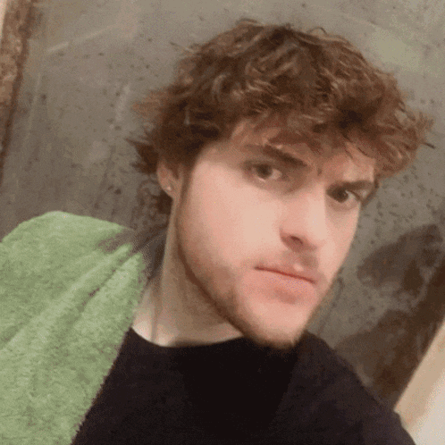 a man with curly hair and a beard is wearing a green towel around his neck