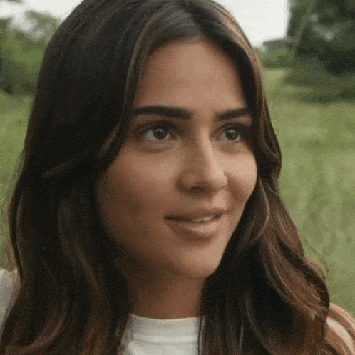 a close up of a woman 's face in a field with trees in the background