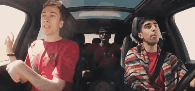 a man wearing a red shirt that says ' eee ' on it is driving a car with two other men