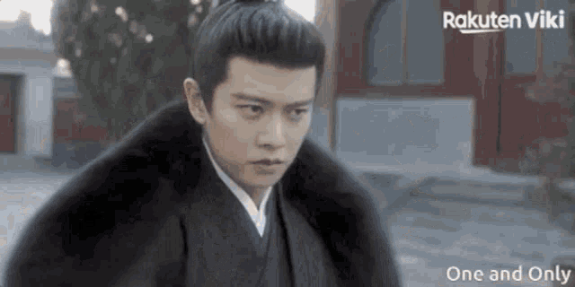 a man in a kimono is standing in front of a building with rakuten viki written on the bottom of the screen .