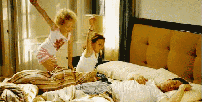 a little girl is jumping in the air while a man sleeps