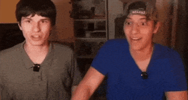 two young men are standing next to each other in front of a camera .