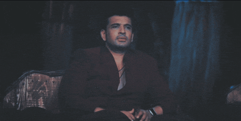 a man in a suit sits on a couch in the dark