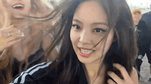 a close up of a woman 's face with her hair blowing in the wind and a man standing behind her .
