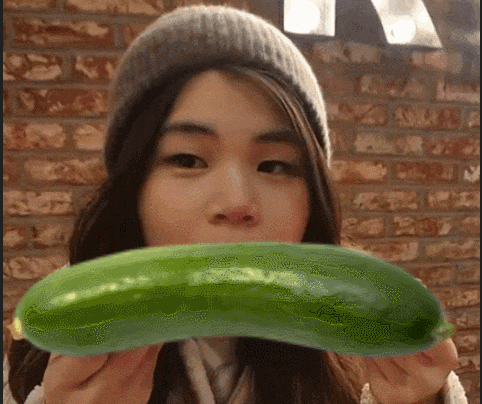 a woman wearing a hat is holding a green cucumber in front of her mouth