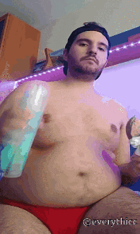 a shirtless man in red underwear is holding a bottle of water