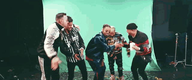 a group of men are standing in front of a green screen