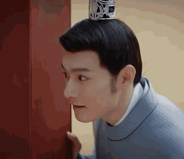 a man with a crown on his head is peeking out from behind a red door .