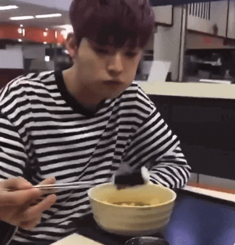 a man in a striped shirt is sitting at a table eating food with chopsticks .