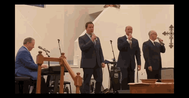 a group of men singing in a church with a keyboard in the foreground and a cross on the wall behind them