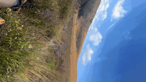 a grassy hillside with a blue sky and clouds behind it