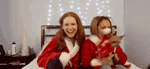 two women dressed in santa claus costumes are sitting on a bed .