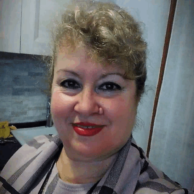 a woman wearing red lipstick and a plaid shirt smiles at the camera