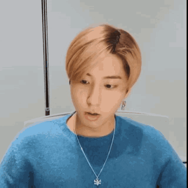 a young man wearing a blue sweater and a necklace with a snowflake pendant