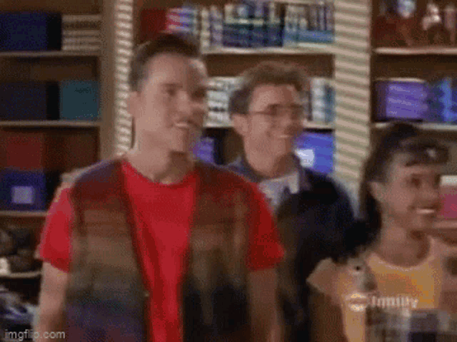 a group of people are standing in a store . one of the men is wearing a red shirt .