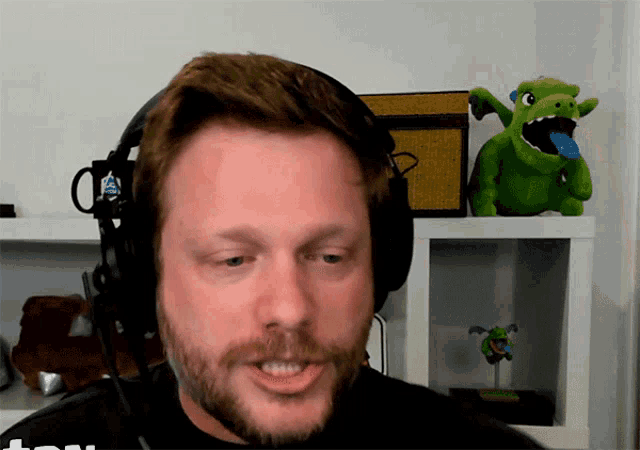 a man wearing headphones with a dragon stuffed animal behind him and a mug that says ' a ' on it
