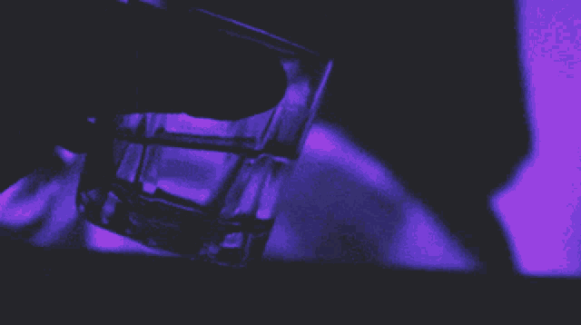 a person is holding a shot glass with a purple light behind them