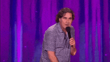 a man is standing on a stage holding a microphone and making a funny face .