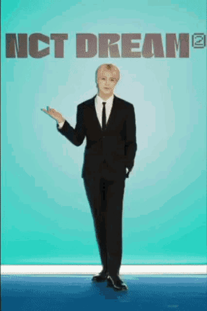 a man in a suit and tie is standing in front of a nct dream poster .