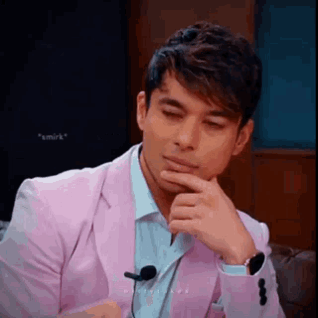 a man in a pink suit and white shirt is sitting on a couch .
