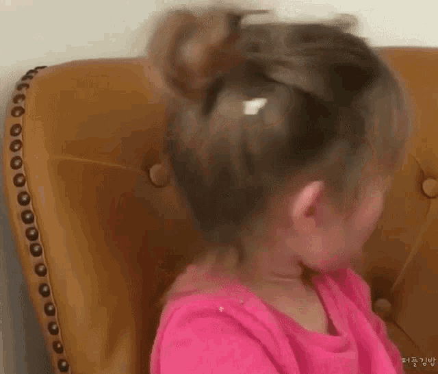 a little girl in a pink shirt is sitting on a chair .