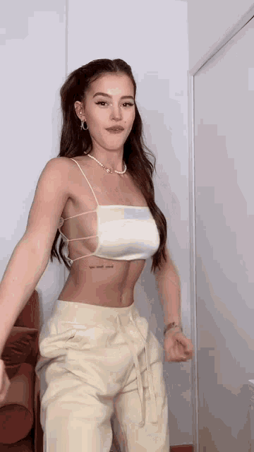a woman wearing a white crop top and beige pants