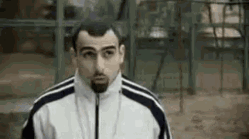 a man with a beard is standing in front of a playground wearing a white and black jacket .