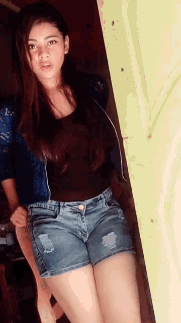 a woman in denim shorts and a black top stands in a doorway
