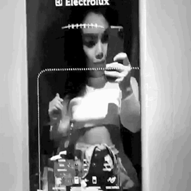a black and white photo of a woman taking a selfie in front of a mirror .