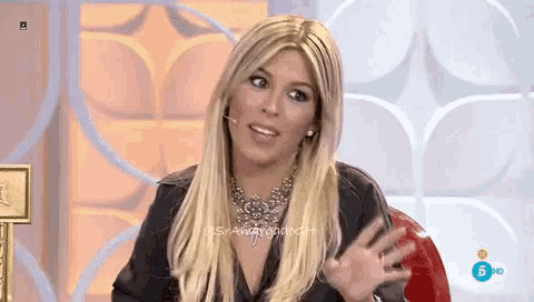 a woman with blonde hair and a necklace is sitting in front of a screen that says 5 hd