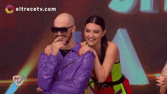 a man in a purple leather jacket is standing next to a woman with eltrecetv.com written on the bottom
