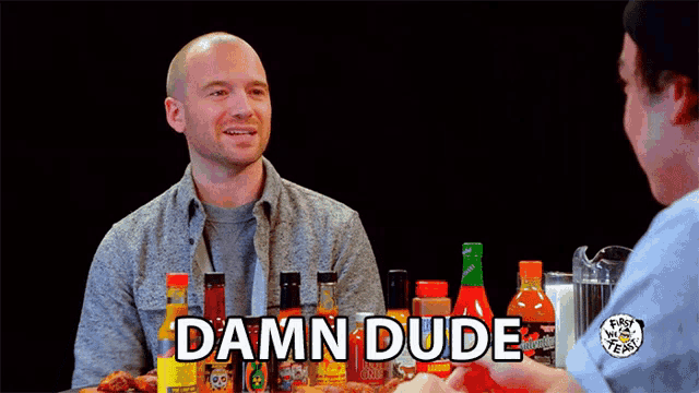 a man sitting at a table with bottles of hot sauce and the words damn dude above him
