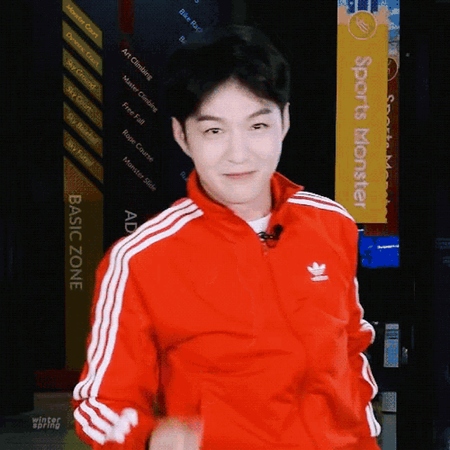 a man wearing a red adidas jacket is standing in front of a sports monster sign