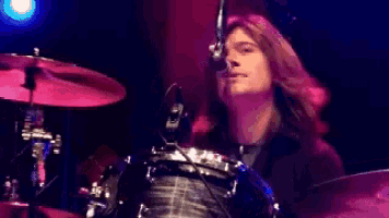 a man with long hair is playing a drum set
