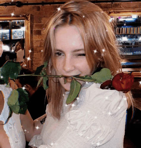 a woman holds a rose in her mouth and winks