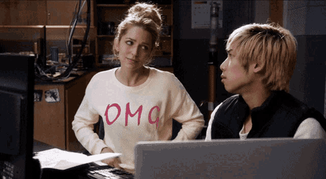 a woman wearing a white omg sweater sits next to a man at a desk
