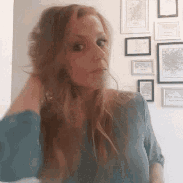 a woman in a blue shirt is standing in front of a wall with framed maps on it