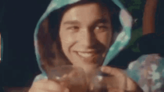 a man is drinking from a glass while wearing a hooded hat .