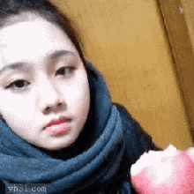 a girl with a scarf around her neck is eating an apple ..