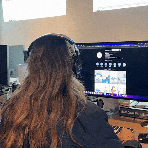 a woman wearing headphones sits in front of a computer with a building in the background