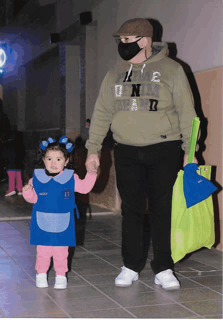 a man wearing a green hoodie with the word n on it holding a little girl 's hand
