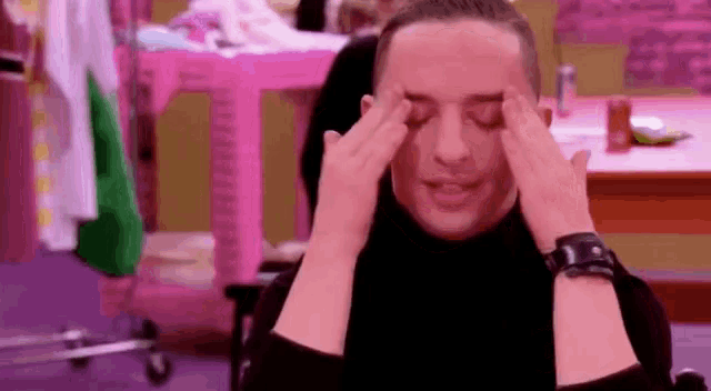 a man is holding his head with his hands while wearing a black turtleneck and a watch .