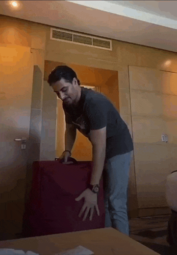 a man in a black shirt is holding a red suitcase in a hotel room