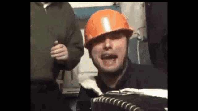a man wearing an orange hard hat is making a face .