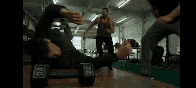 two men are fighting in a gym with a dumbbell in their hand .