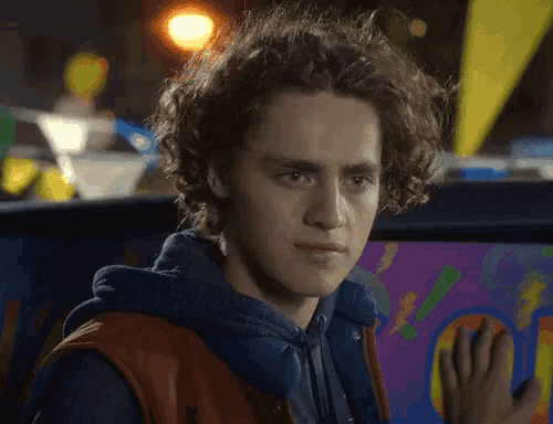 a young man with curly hair stands in front of an arcade machine
