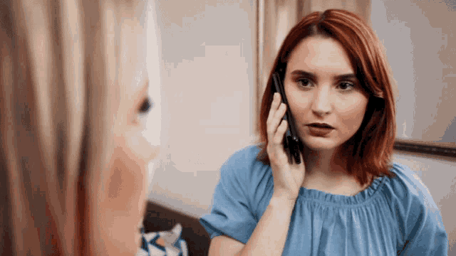 a woman with red hair is talking on a cell phone with another woman