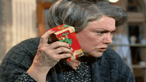 an elderly woman is holding a small red box with a christmas tree on it