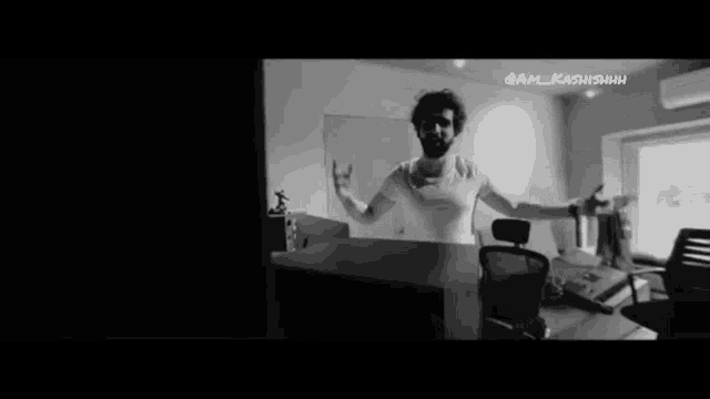 a black and white photo of a man standing in a room with his arms outstretched .
